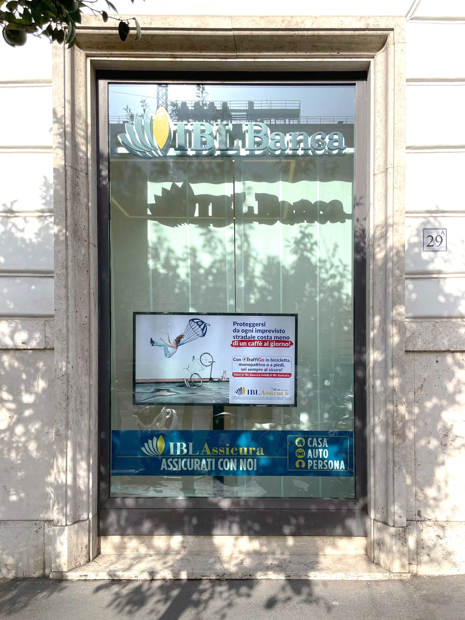 A vertical monitor in an IBL Banca window showing an IBL Assicura insurance campaign